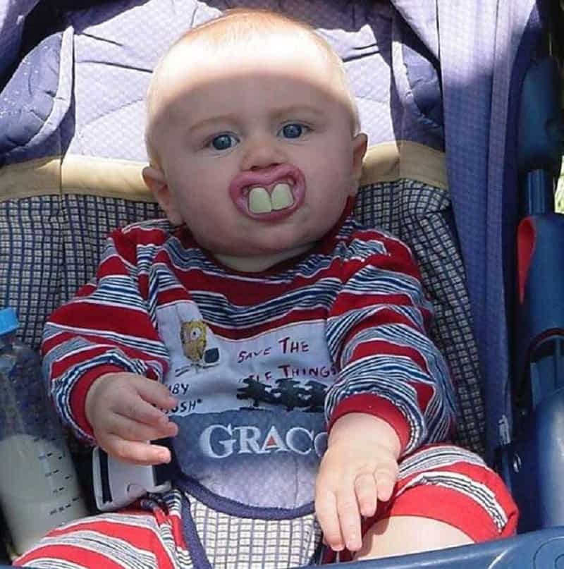 Seorang bayi mengenakan gigi palsu di mulut, bikin lucu.